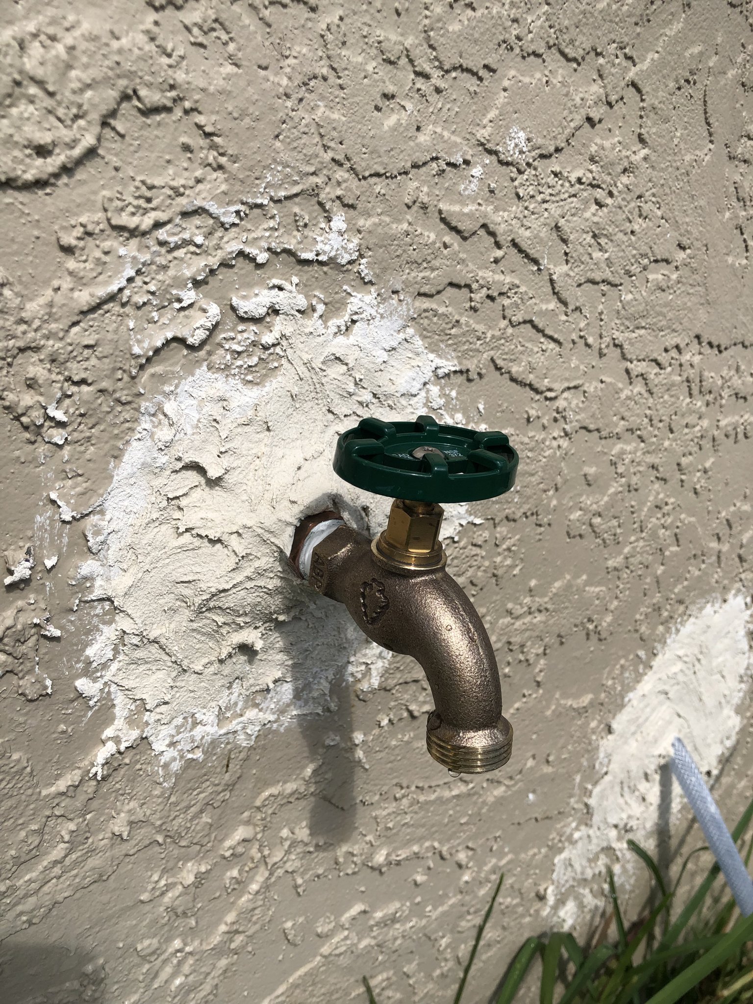 Brass hose bib with a green wheel handle on a textured stucco wall of a Palm Coast house