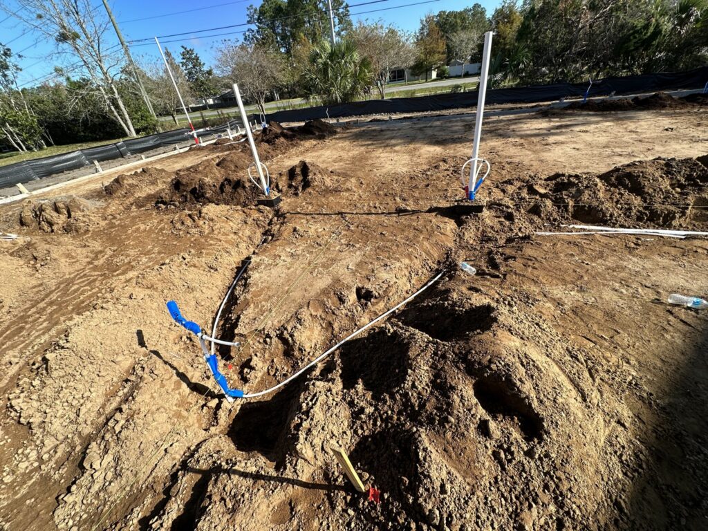 Underground PVC drain risers and blue water lines in a trenched building pad before a Palm Coast slab pour