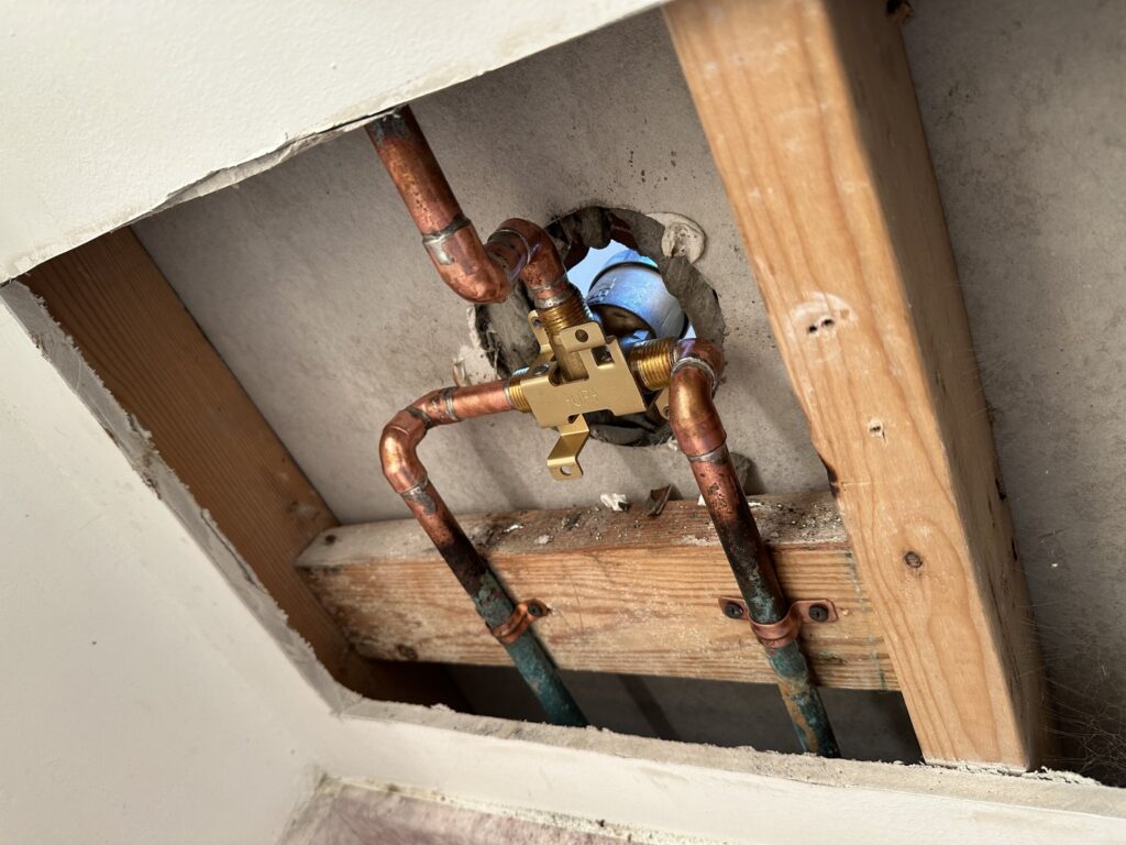Copper plumbing supply lines and a shut-off valve exposed inside a cut-out wall during a plumbing repair