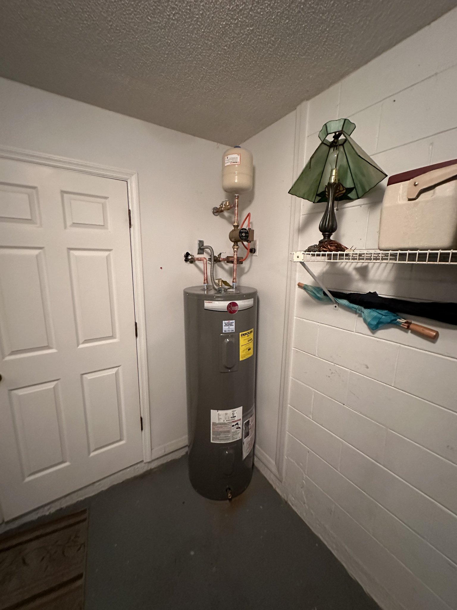 Electric tank water heater standing in a utility closet next to a white door