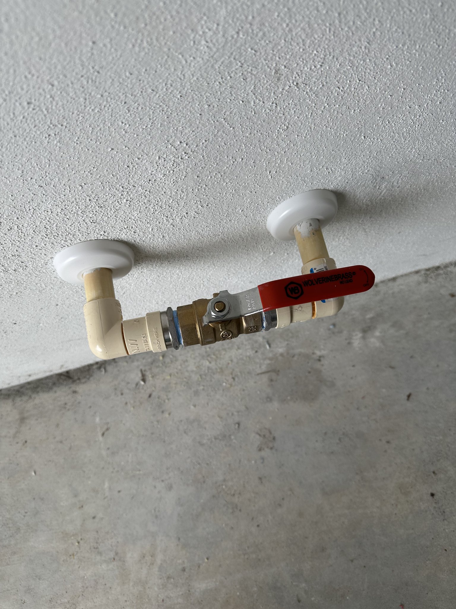 Pair of shutoff valves with red handles on supply pipes coming out of a wall