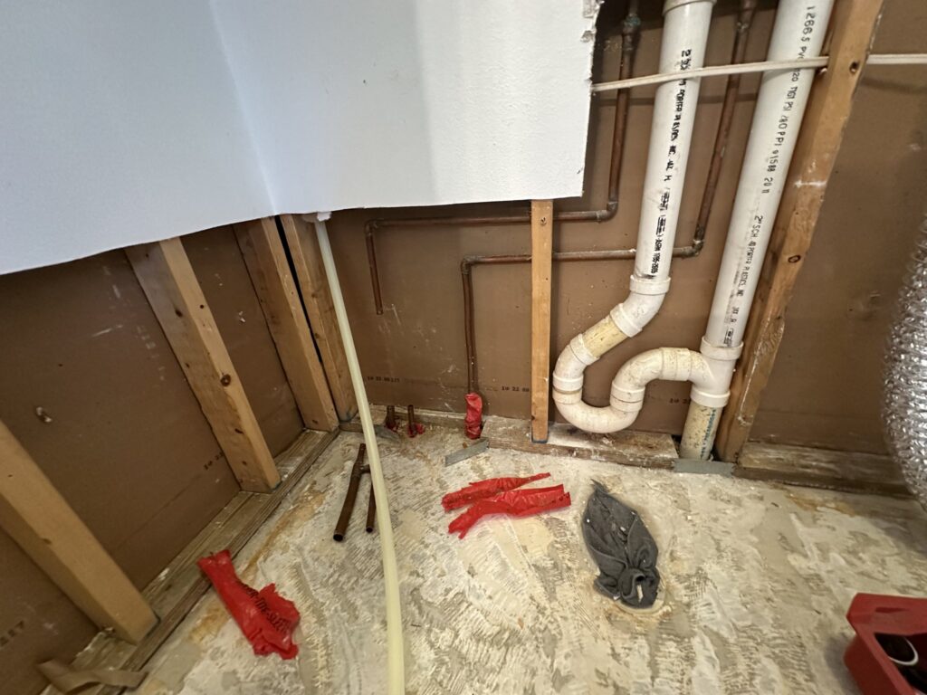 Open wall cavity with exposed white drain pipes and a P-trap during plumbing rough-in work