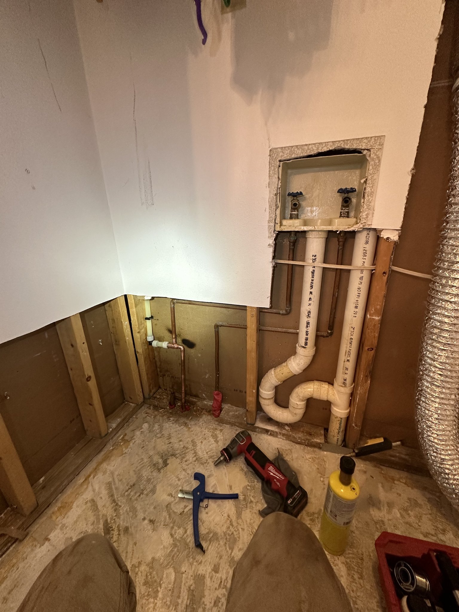 Open wall with drain piping and supply lines exposed during a plumbing job